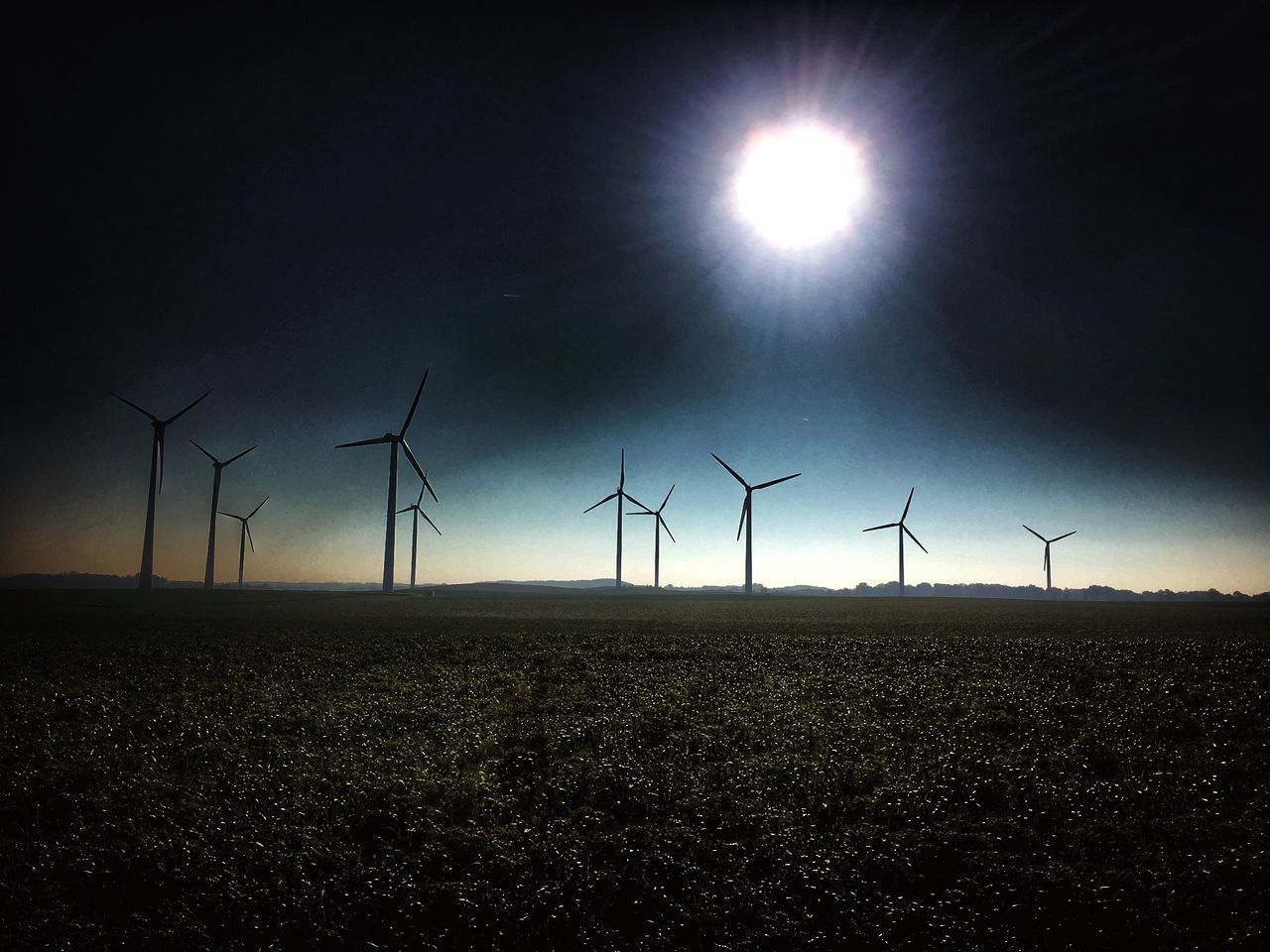 WIND TURBINES ON FIELD AGAINST BRIGHT SUN