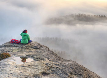 Rear view of man sitting on rock against mountain