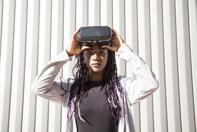 Excited young african american female in vr headset entertaining and playing virtual game against gray striped wall