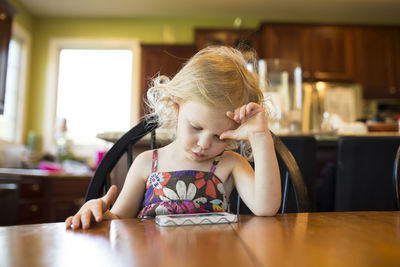 Girl looking at mobile phone while sitting on chair by table at home