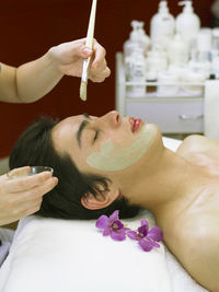 Cropped hands of massage therapist applying facial mask to man