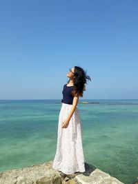 Full length of woman standing on rock at sea against clear blue sky