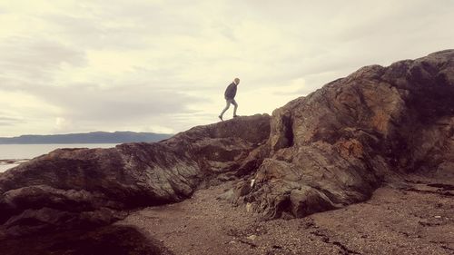 Man on rock at beach against sky