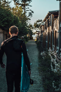 Rear view of man with surfboard walking on footpath in city