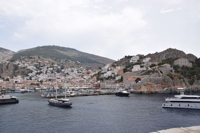 Sailboats in sea by townscape against sky