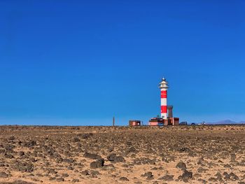 Lighthouse on field by building against clear blue sky