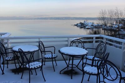 Snow covered chairs and tables at outdoor cafe against sky during winter