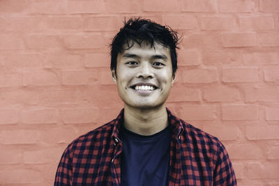 Portrait of young man standing against brick wall