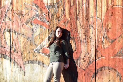 Beautiful woman standing against graffiti on wooden wall