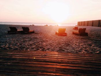 Lounge chairs at beach against sky during sunset