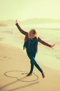 Full length of woman posing on heart shape at beach against sky