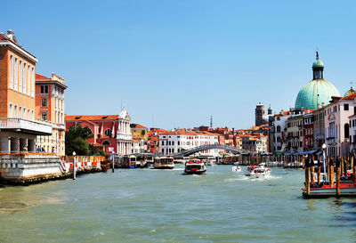 Boats moving on grand canal amidst buildings against clear blue sky