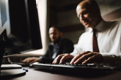 Senior businessman typing on keyboard while using computer by male colleague at desk in law office