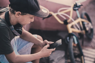 Boy using phone while sitting by bicycle