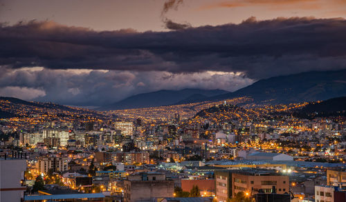 Illuminated cityscape against cloudy sky at dusk