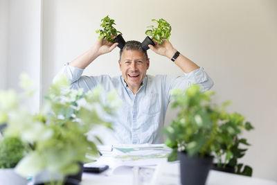 Playful man holding potted plants at home