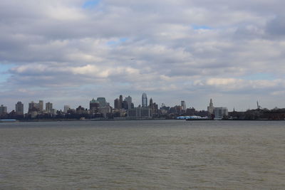 Sea and buildings in city against cloudy sky