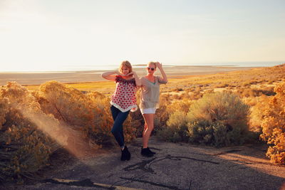 Full length of friends posing at beach against sky