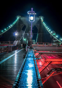 People on illuminated bridge against sky at night