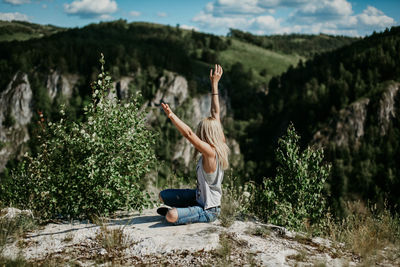 Man with arms raised against trees and mountains