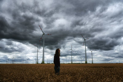Man standing on field by windmills against cloudy sky