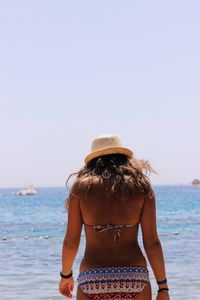 Rear view of young woman standing at beach against clear sky