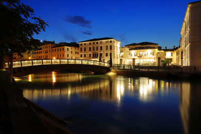 Illuminated buildings by river against sky in city at dusk