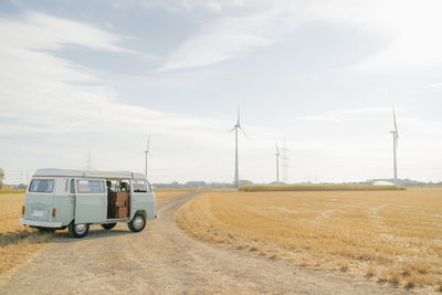 Camper van parked on dirt track in rural landscape with wind turbines