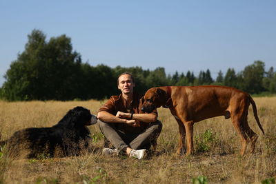 Man with dogs sitting on grass against sky