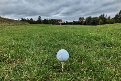 Close-up of golf ball on field against cloudy sky