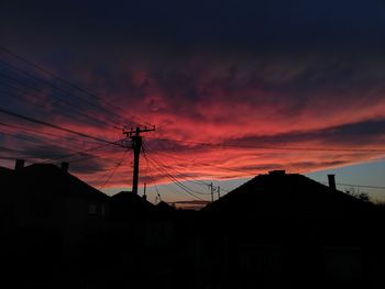 Silhouette houses and electricity pylon against sky during sunset