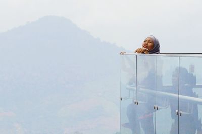 Mother and daughter standing in balcony against mountains during foggy weather