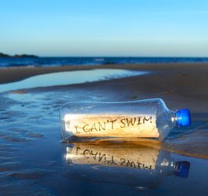 Bottle with message at beach against blue sky