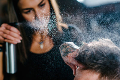 Close-up of woman spraying on man hair