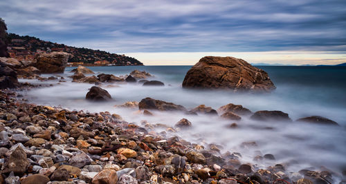 Rocks in sea against sky during sunset