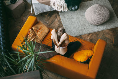 An overhead view of a woman sitting on a sofa in her home in a lotus position and practicing yoga 