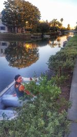 Rear view of woman sitting by lake against sky