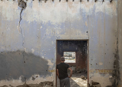 Rear view of adult man standing in doorway of an abandoned building