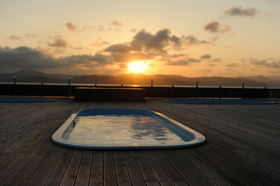 Blue small pool with water on wooden deck against the background of the sea and sunset