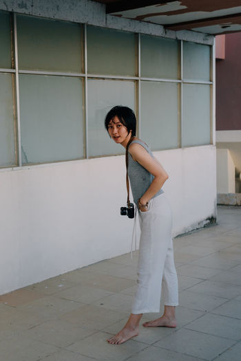 FULL LENGTH PORTRAIT OF WOMAN STANDING AGAINST BUILDING