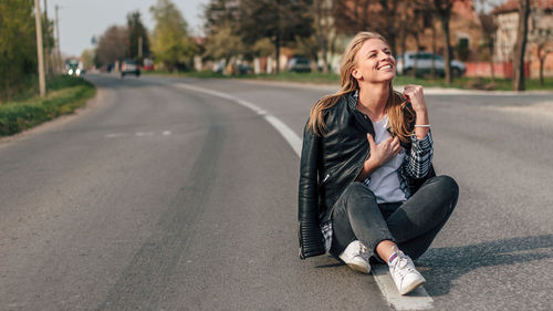 Portrait of smiling young woman sitting on road in city