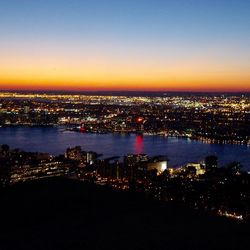 Illuminated city at waterfront during sunset