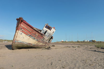 Abandoned boat moored on beach against clear sky