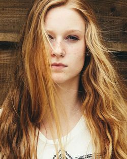 Close-up portrait of serious young woman by wooden wall