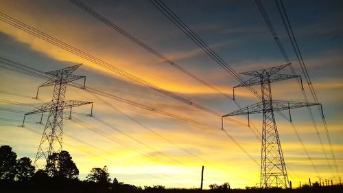 Low angle view of electricity pylon against sky during sunset