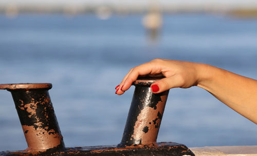 Close-up of hand against sea against sky