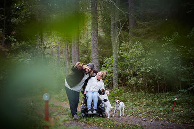 Young male caretaker taking selfie with disabled woman in wheelchair at forest