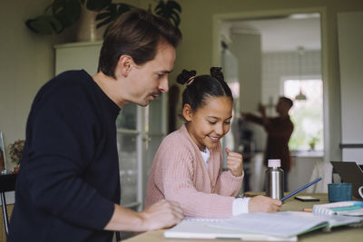 Father sitting next to excited daughter doing homework at home