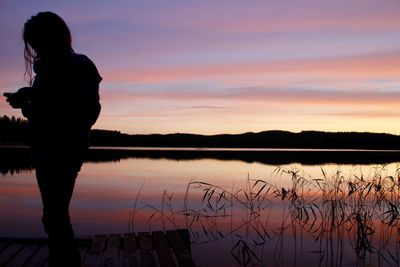 Silhouette man standing by lake against sky during sunset