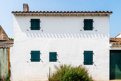 White facade with green windows with closed shutters of traditional house decorated with flowers